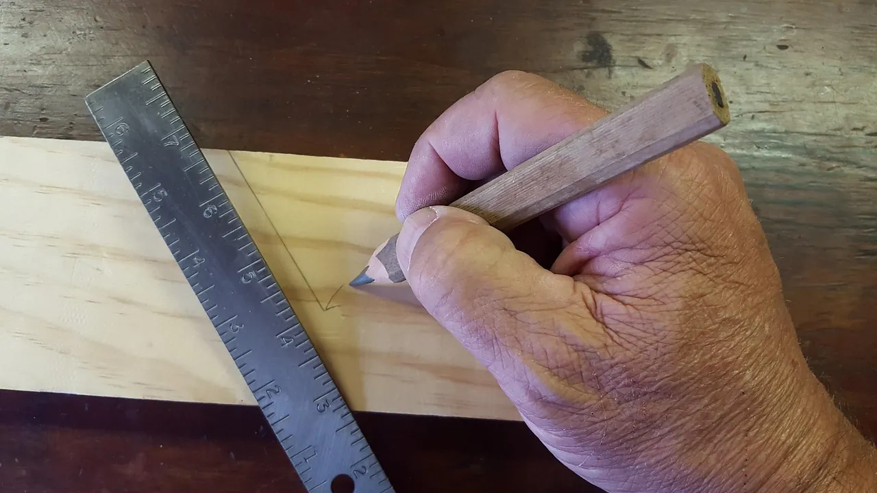 Main qui trace un trait au crayon le long d’une règle en acier sur une planche